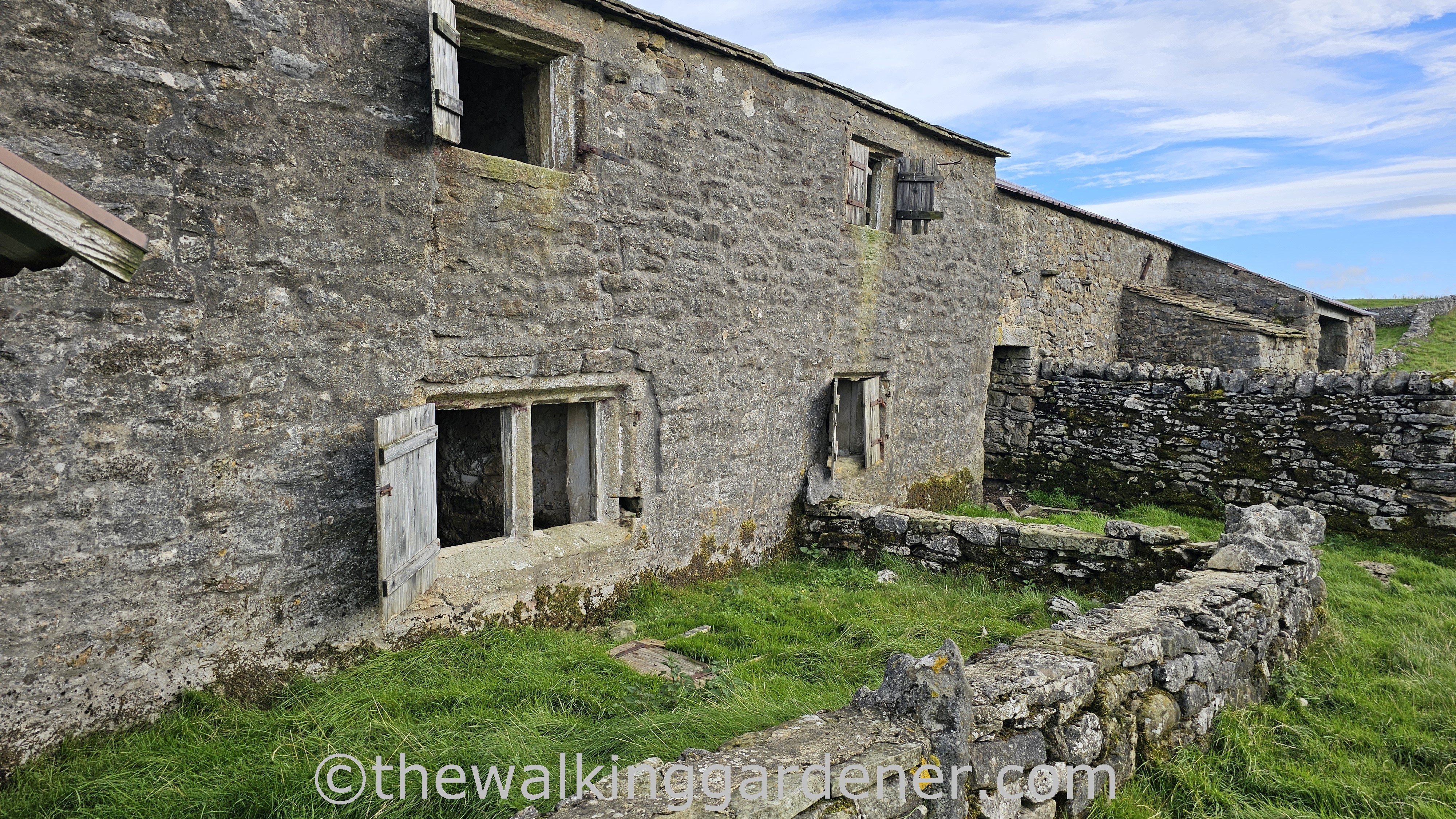 An abandoned farmhouse - Bare House - with weathered stone walls and boarded windows, surrounded by overgrown grass and a low stone wall.