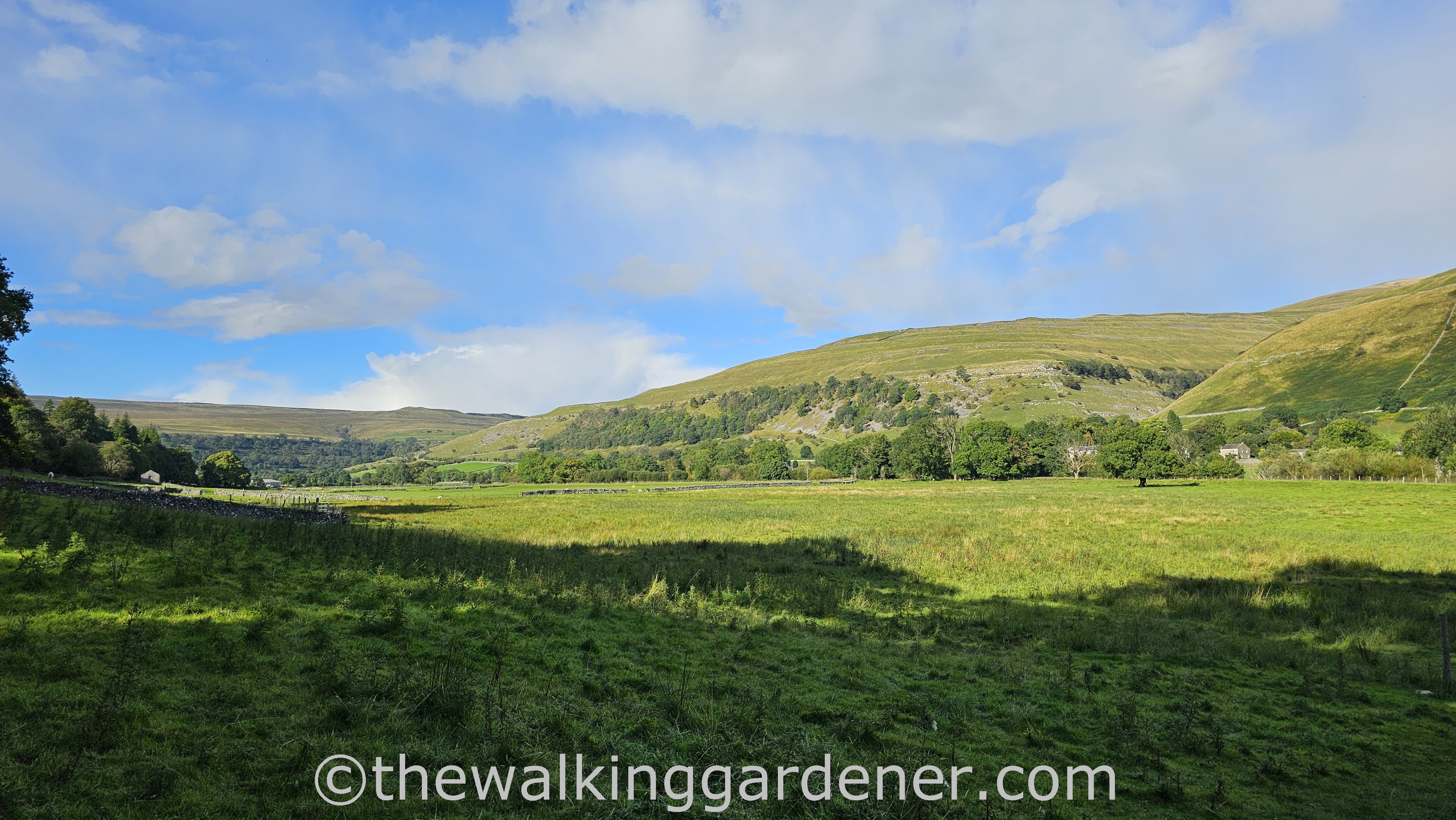 A picturesque view of a green valley surrounded by rolling hills under a blue sky with scattered clouds.