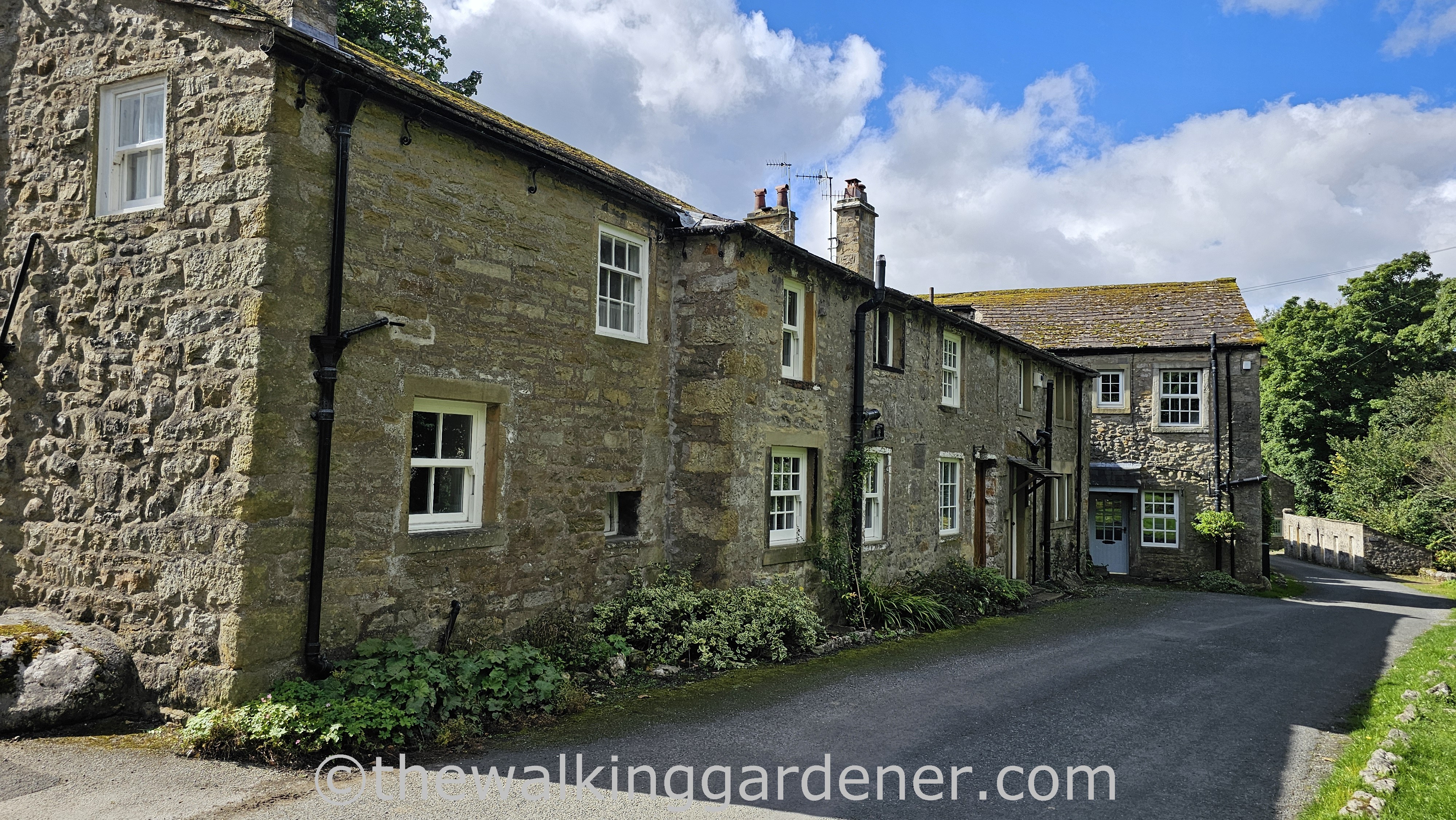 A row of charming, traditional stone houses in Kettlewell with lush greenery lining the path in a rural setting.